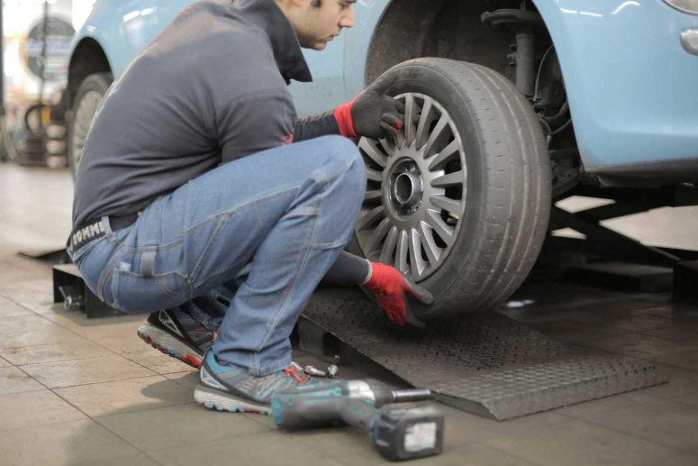 Mechanic removing car tyre from wheel hub inside automotive workshop